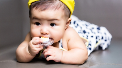 Cute happy asian baby sucking nipple pacifier laying on sofa, 5 months after birth
